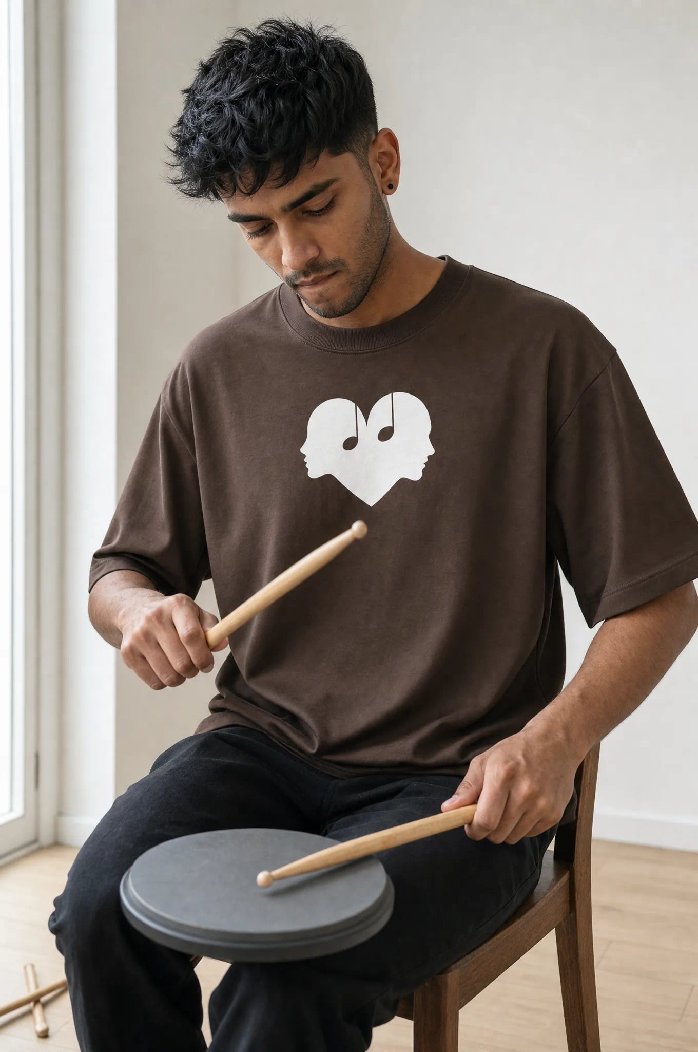 Man practicing drums in the Mocha Overture Oversized Tee